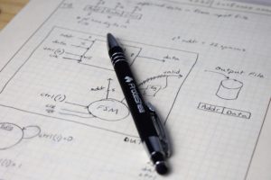 pen laying across engineering paper that has multiple schematics on it