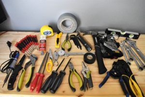 Layout of tools which includes a tape measure, screwdrivers, duct tape, pliers, files, vise grips, caliper, level, soldering iron, hammer, and box cutter